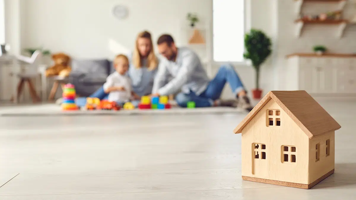 La maison unifamiliale de vos rêves : le bonheur de toute la famille Famille heureuse avec bébé en arrière-plan flou et maison en bois miniature au premier plan